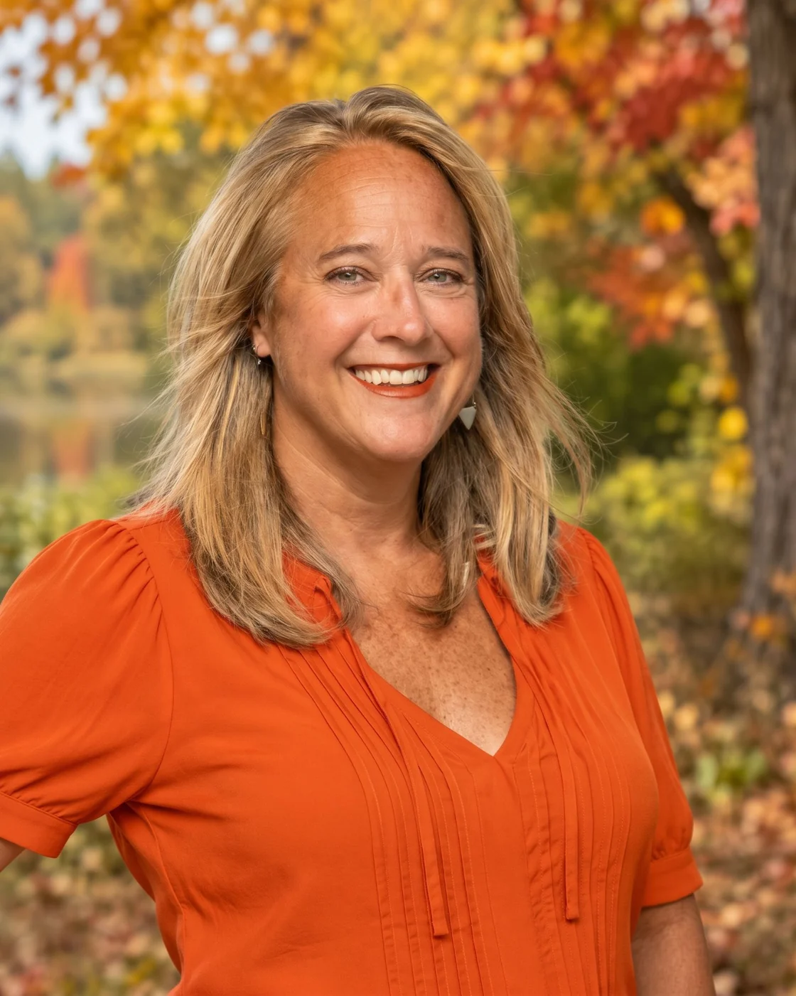 Suzanne Deatherage smiling outdoors in front of fall foliage